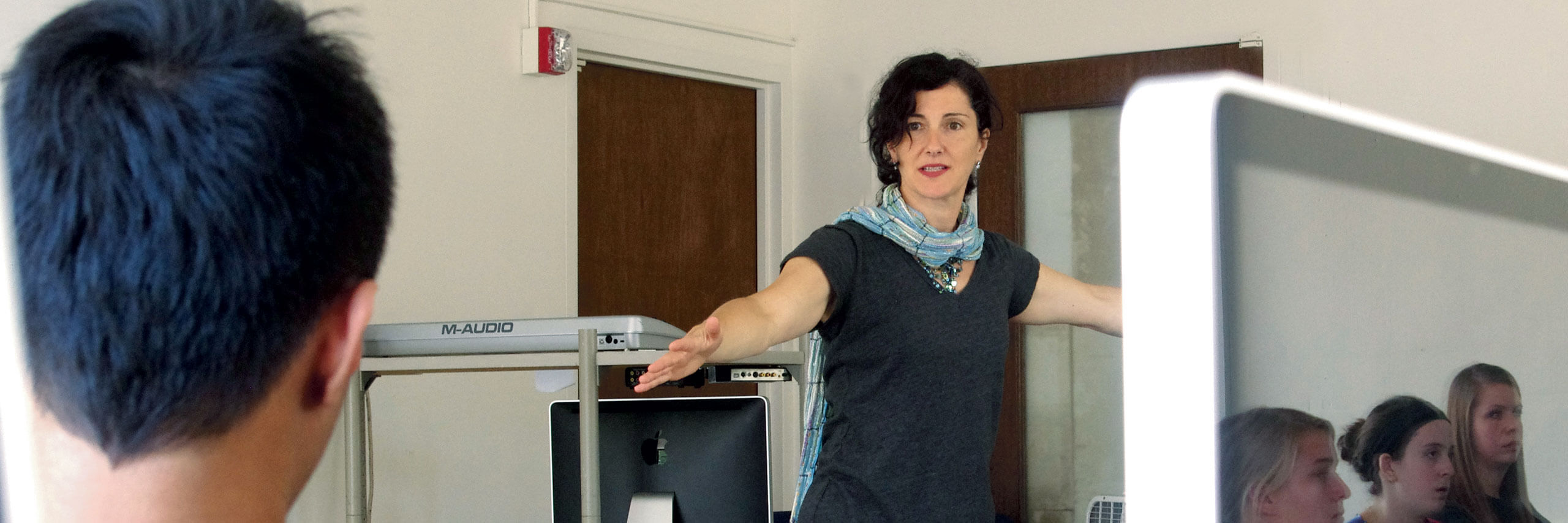 A professor lectures to students while they work on their computers.