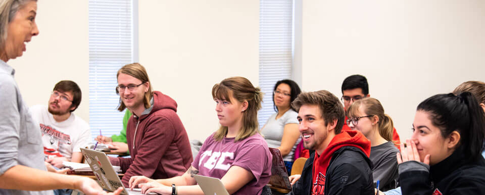 Students in a classroom smile towards their professor.