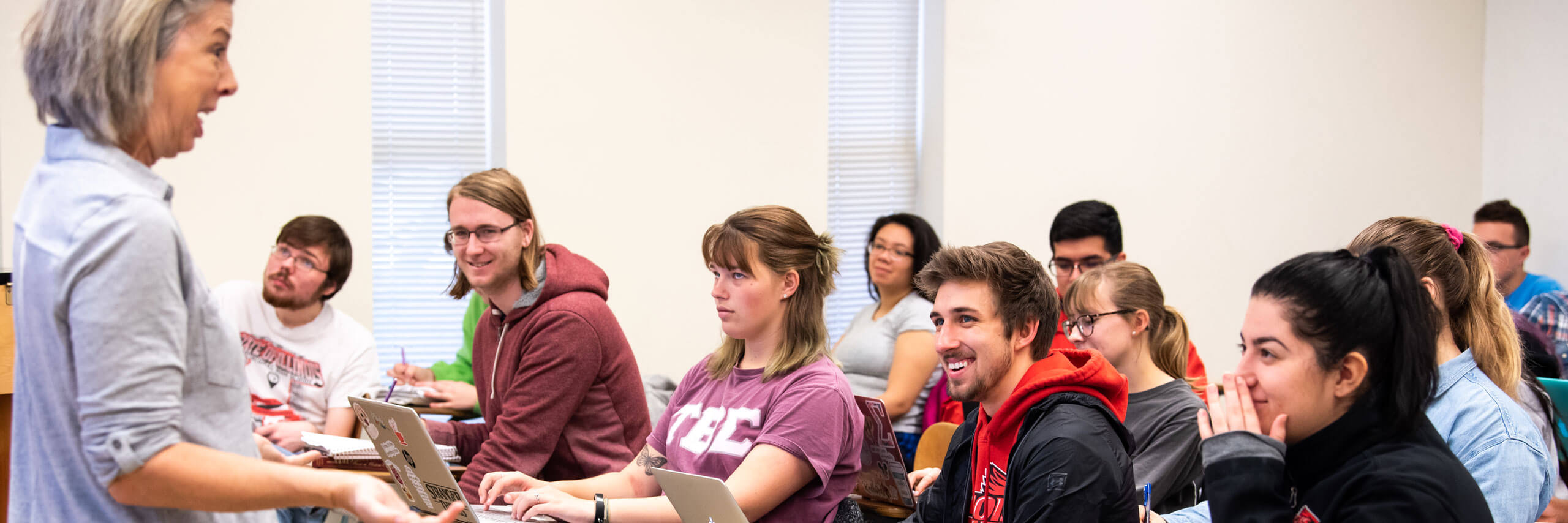 Students in a classroom smile towards their professor.