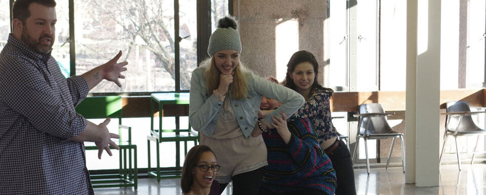 A teacher and his students rehearse a skit during class.